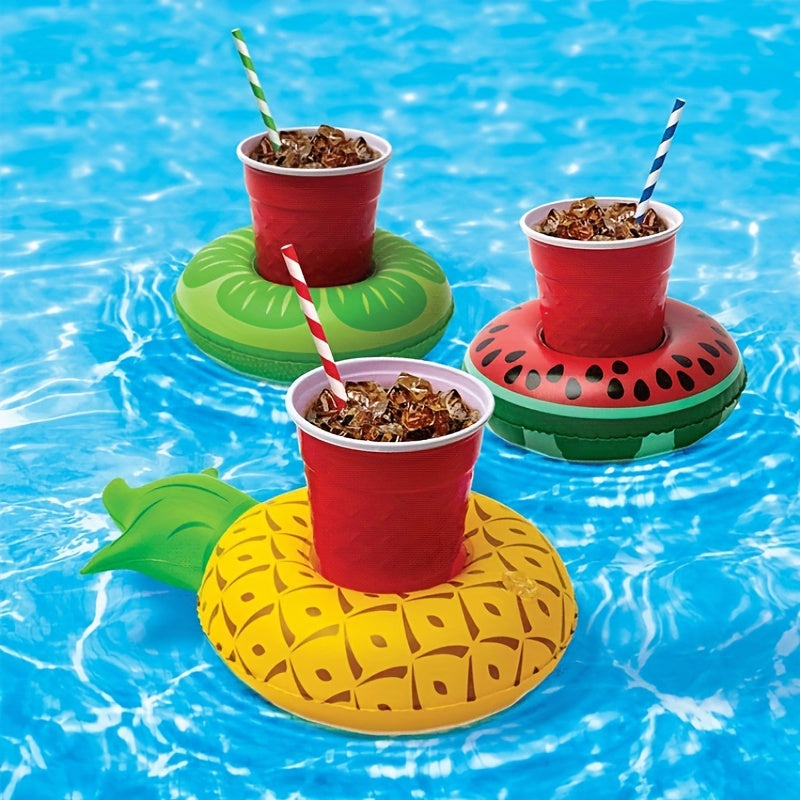 Four colorful Flashfy inflatable drink holders with red cups filled with a dark liquid, including pineapple, watermelon, and leaf designs, on a pool.